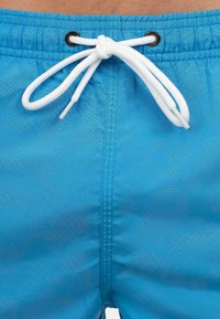 Costume da bagno blu realizzato in tessuto leggero con vita elastica, dotato di un laccio bianco e occhielli in metallo per la regolazione.