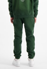 Groene, gezellige sweatshirt en bijpassende joggers, voorzien van ribgebreide manchetten en een elastische tailleband, gecombineerd met witte sneakers. Zachte, gestructureerde stof.
