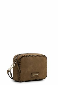 Brązowa zamszowa torebka crossbody ze złotymi detalami, z kontrastowym przeszyciem wzdłuż brzegów i zamknięciem na zamek u góry.