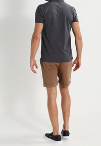 Polo shirt gris foncé, shorts beige avec des manches retroussées et chaussures noires à enfiler. Pas de détails de marque visibles. Design simple et décontracté.