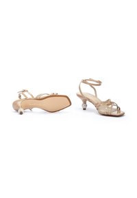 Sandalias estrapadas beige con tacón bajo, que presentan un acabado texturizado y un detalle decorativo de strass en el tacón. Correa ajustable en el tobillo.