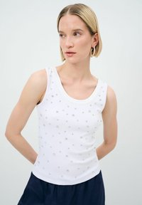Top bianco senza maniche con scollatura rotonda, decorato con piccoli strass sparsi. Tessuto morbido e design aderente.