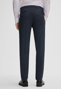 Navy blauwe tekstuur broek met rechte pijpen, twee achterzakken en een tailleband, gecombineerd met een witte blouse met lange mouwen.