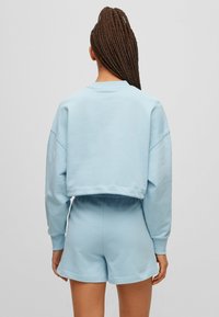 Sudadera recortada de color azul claro con hombros caídos, combinada con pantalones cortos a juego. Tejido suave y cinturilla elástica, con un ajuste relajado.