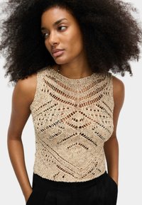 Béžový pletený crop top s otevřenými geometrickými vzory, širokým výstřihem a bezrukávovým provedením; texturovaná látka s volným střihem.