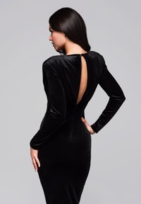 Robe en velours noir avec un col montant, des manches longues et un dos ouvert. Texture lisse, silhouette ajustée et détail de fermeture discrète au dos.