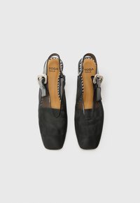 Chaussures slingback noires avec un bout pointu, des côtés en maille transparente et une grande boucle décorative sur la sangle. Semelles intérieures en cuir lisse.