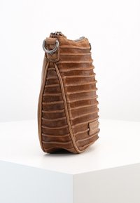 Brązowa zamszowa torba z pionowymi rowkami, zaokrągloną podstawą i zapięciem na zamek. Posiada srebrne akcesoria oraz subtelną metkę marki z boku.