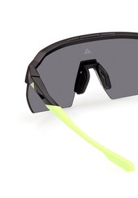 Sportssolglasögon med svart ram, mörka linser och klara gröna örontips. Designen har en geometrisk form och texturerade sidor.