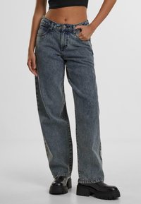 Kõrge vöökoht, laiad sinised denim püksid, millel on kulunud viimistlus, viis taskut, vöölõngad ja nähtav õmblus. Kombineeritud turskete mustade saapadega.