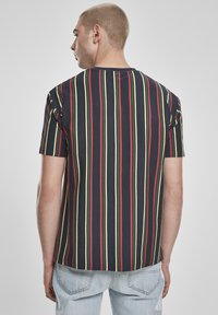 Rövid ujjú ing, vertikális piros, zöld és sárga csíkokkal sötét alapon, kerek nyakkivágással és laza szabással.