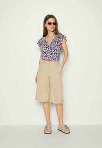 Blusa de manga curta com padrão floral em azul-marinho e branco, combinada com calções beiges até ao joelho. Sandálias com detalhe de fivela completam o conjunto.