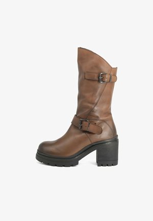 Stivale marrone in pelle, alto fino al ginocchio, con punta appuntita, due fibbie e un tacco impilato nero dalla texture. Caratterizzato da una suola in gomma robusta e una finitura liscia.