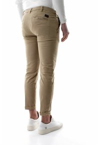 Chinos beige con vestibilità slim, orli arrotolati e due tasche posteriori, abbinati a sneakers bianche. Tessuto misto cotone, texture liscia.