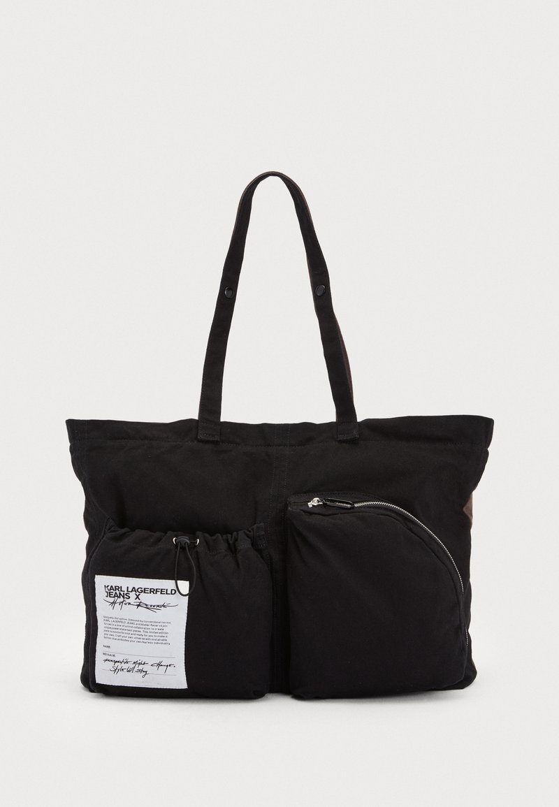 Bolsa de lona preta com dois bolsos frontais, um com fecho e outro com cordão. Inclui etiqueta de marca no bolso maior. Alças para transporte fácil.