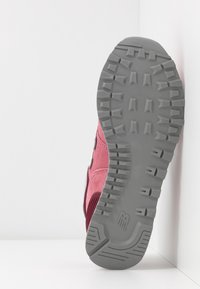 Růžové semišové tenisky s šedým gumovým podešvem. Podešev má texturovaný vzorovaný povrch pro lepší trakci. Na boku se nachází bílé akcenty.