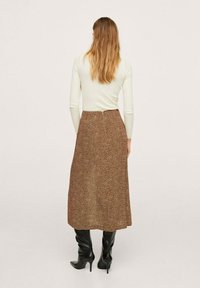 La falda midi marrón presenta un patrón de puntos, con un diseño de cintura alta y una textura suave. Se combina con botas negras hasta la rodilla.