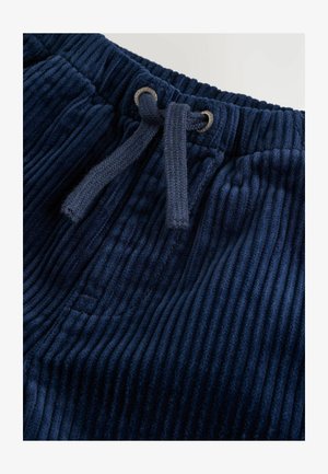 Navy corduroy-housut, joissa on nauhavyötärö, näyttäen hienoa ribbed-tekstuuria ja hopeisia silmukoita vyötäröllä.
