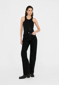 Top black senza maniche con decorazioni abbinato a jeans neri a vita alta. Modella che indossa stivaletti neri con tacco.