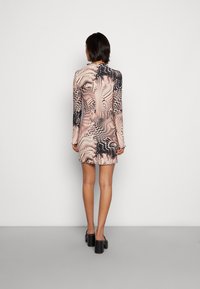 Robe mini à manches longues dans un motif abstrait rose et noir, avec un design ajusté, un tissu texturé et un ourlet volanté. Talons épais noirs.