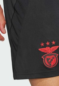 Pantalones cortos deportivos negros con una tela texturizada, y un destacado logo bordado en rojo en la parte inferior izquierda.