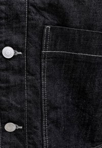 Tamno traper jakna prikazana izbliza, srebreni brandirani gumbi i našiveni pravokutni prednji džep bijelim koncem.