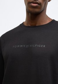 Czarny bawełniany t-shirt z okrągłym dekoltem i szarym logo "TOMMY HILFIGER" na piersi. Gładka faktura, minimalistyczny design.
