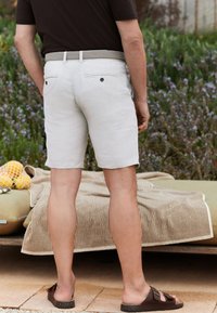 Light-colored, knee-length shorts made of linen, featuring two back pockets. Worn with a braided belt and slip-on sandals.