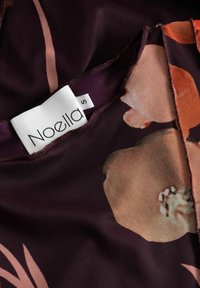 Kwiatowy materiał w głębokim burgundzie z jasnoróżowymi i pomarańczowymi wzorami; posiada metkę z napisem "Noella" i rozmiarem "S" w okolicy dekoltu.
