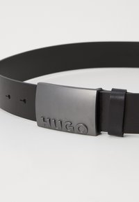 Zwarte leren riem met een rechthoekige zilvergrijze gesp met reliëf "HUGO"-logo. Gladde textuur met een minimalistisch ontwerp en twee verstelgaten.