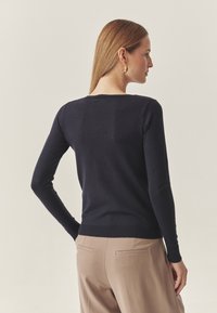 Laivastonsininen pusero, jossa on istuva malli ja pitkät hihat, valmistettu sileästä kankaasta. Siinä on resorireunus helmassa ja niskan takana. 