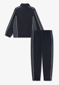 Σκούρο μπλε φόρμα με ζακέτα που κλείνει με φερμουάρ και παντελόνι με ελαστική μέση. Διακοσμημένη με λεπτομέρειες σε ανοιχτό χρώμα κατά μήκος των ραφών και των μανσετών.