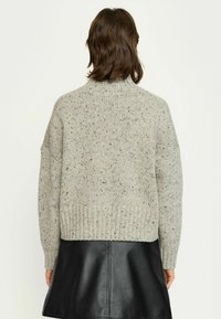 Pulover gri din tricot cu guler înalt, având o textură pătată. Puloverul are mâneci supradimensionate și o margine cu model în relief, asortat cu o fustă neagră din piele.