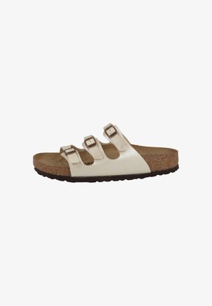 White slide sandal with three adjustable buckled straps, cork footbed, and textured black sole, side view.