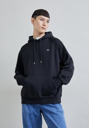 Hanorac negru cu glugă, cu buzunar frontal, logo alb pe piept și șnururi ajustabile. Asortat cu blugi din denim de culoare albastră deschisă.