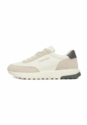 Flacher beige-cremefarbener Calvin Klein Sneaker mit Wildlederpanels, Schnürdesign und schwarzem Fersenakzent auf weißer Sohle mit profiliertem Außensohle.