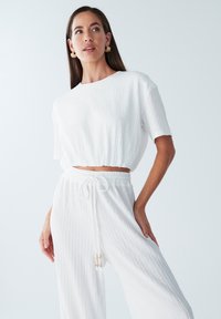 Witte cropped top en brede broek van gestructureerde stof, met een elastische tailleband met trekkoord en decoratieve kralen.