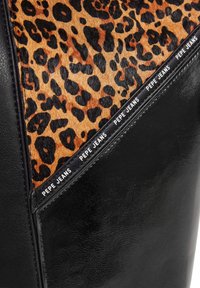 Svart läderväska med en leopardmönstrad panel. Designen har en texturerad yta och en tryckt logostrip längs kanten.