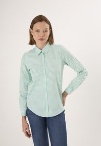 Chemise à carreaux vert clair avec un col, des manches longues et un ourlet arrondi, associée à un jean bleu.