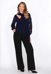 Granatowy sweter dzianinowy z koronkowymi rękawami, z wycięciem, w zestawie z czarnymi szerokimi spodniami i czółenkami z ostrymi noskami.