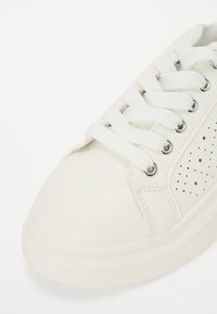 Białe skórzane sneakersy z okrągłym noskiem, sznurowanym zapięciem oraz perforowanym detalem po bokach. Płaska biała gumowa podeszwa z przeszyciem wzdłuż krawędzi.