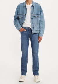 Denimjacka i ljusblått, med två bröstfickor, knappfront och avslappnad passform; kombinerad med slim fit blåjeans och vita sneakers.