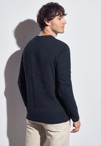 Long-sleeve, dark navy T-shirt with a textured fabric. Features a rounded neckline and a relaxed fit, paired with light-colored pants.