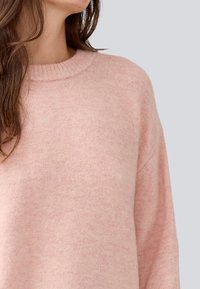 Pull en rose clair en tissu doux, avec un col côtelé et des coutures d'épaule légèrement abaissées pour un ajustement décontracté.