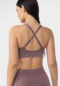 Bralette ajustado en suave, elástico y apagado tono malva. Cuenta con tirantes cruzados ajustables y una banda inferior ancha para mayor soporte.