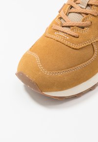 Hnědé semišové tenisky s kulatou špičkou, strukturovanými hnědými tkaničkami, světle šitými akcenty a bílou střední podrážkou a hnědou gumovou podrážkou.