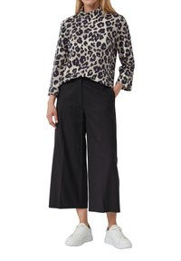 Top con stampa leopardo in beige e blu navy, con collo alto e maniche a tre quarti, abbinato a pantaloni a gamba larga neri e sneakers bianche.