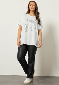 Hvid kortærmet t-shirt med et metallic blomstermotiv, parret med sorte bukser i faux læder og hvide sneakers. Glat stoftekstur.