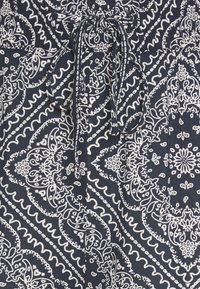 Námorně modrá tkanina s bílými paisley a květinovými vzory, obsahující stahovací šňůrku a texturované povrchové detaily.