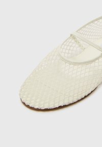 Chaussure plate en maille blanche avec un bout arrondi, une lanière fine sur le cou-de-pied, une surface texturée et une semelle lisse.